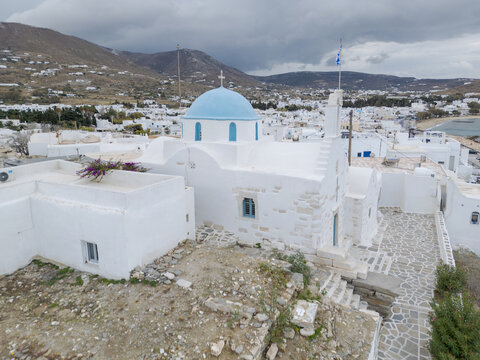 Aerial view of a whitewashed church with a striking blue dome piercing the sky, a beacon of serenity against the rugged landscape, Paros, Paros, Greece.