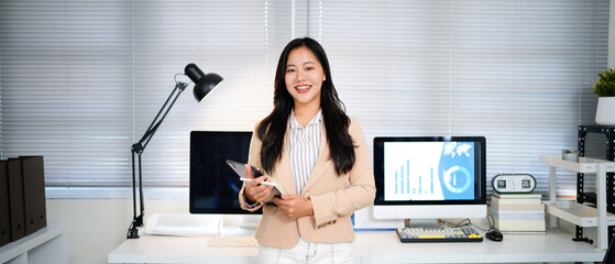 Portrait of young Asian professional business woman standing in office. Happy female company executive, smiling businesswoman entrepreneur corporate leader manager looking at camera using tablet