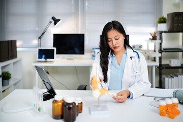 Asian Woman Doctor at Desk with Spinal Model tablet in Clinic for Healthcare Treatment Analysis and Patient Education Explaining Diagnosis