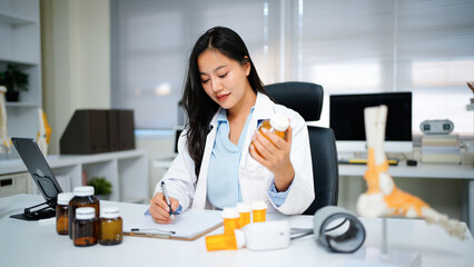 Woman doctor reviews medication bottle while writing notes in a sunlit clinic room suggesting a...