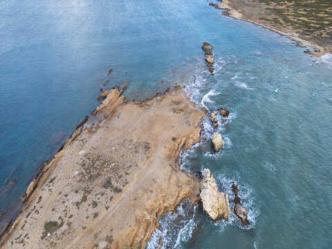 Aerial view of the rugged coastline where tan earth meets the turquoise sea, Paros, Paros, Greece.