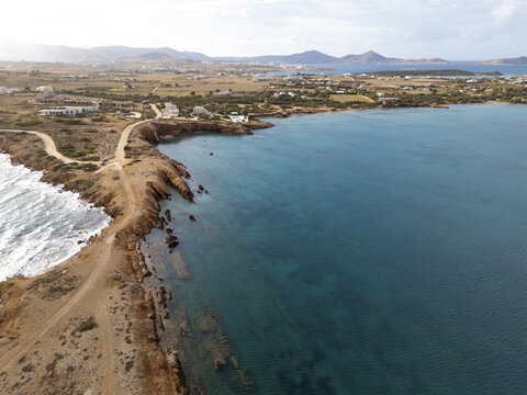 Aerial view of the rugged coastline where the land meets the turquoise sea, a tranquil path winding along the cliffs, Paros, Paros, Greece.