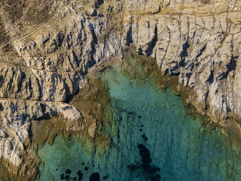Aerial view of the rugged coastline where the pale cliffs meet the shimmering turquoise sea, a dance of raw earth and vibrant water, Paros, Paros, Greece.