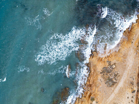 Aerial view of turquoise waves crash against the golden shore, creating a stunning contrast of colors along the coastline, Paros, Paros, Greece.