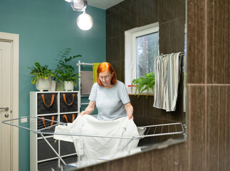 A senior female meticulously straightens the fabric of her washed clothes on a household drying rack to promote wrinkle-free drying results.