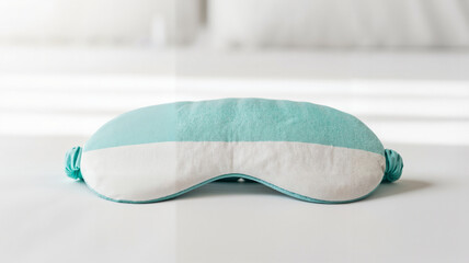 Soft turquoise sleep mask on white bed linens in bright room  