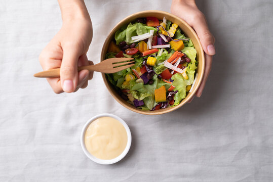 Healthy vegetable salad with lettuce, tomato, pumpkin, corn, purple sweet potato, cabbage, azuki bean and crab stick in takeout bowl eating with salad dressing, Top view