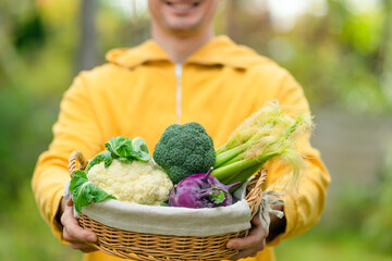 Smiling man farmer proudly holding basket with cauliflower, kohlrabi, broccoli, and corn. Harvest season and organic farm vegetables for healthy food.