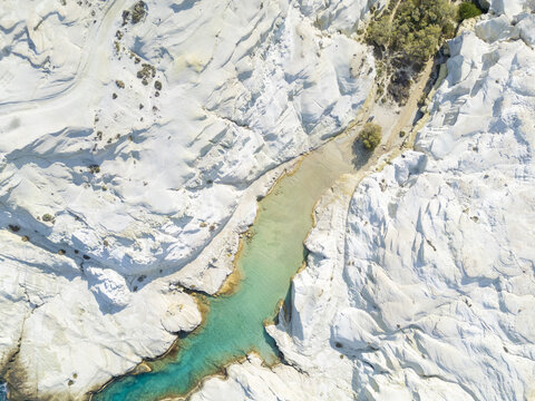 Aerial view of a striking contrast of turquoise waters cutting through the stark white, lunar landscape of Sarakiniko Beach, Milos, Anatoliki Attiki, Greece.