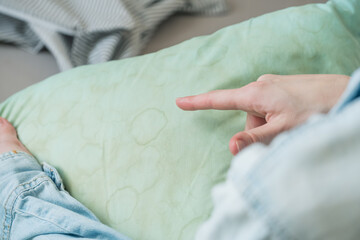  Human finger points at dirty yellow stains sweat or saliva on a green pillow in a living room....
