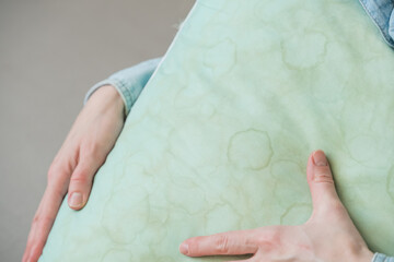 Female hands showing pillow in a living room. Dirty stains sweat or saliva on a green pillow. Conscious home care and sustainable living concept. top view