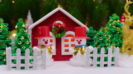 A house surrounded by snowmen and Christmas trees behind a fence against a backdrop of large Christmas tree branches