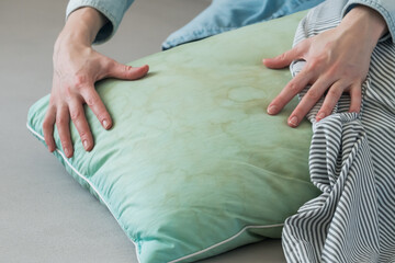 Female hands removing pillowcase from pillow in a living room. Dirty stains sweat or saliva on a green pillow. Conscious home care and sustainable living concept. Side view
