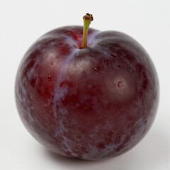 Obraz premium Fresh plum photographed in natural light, perfectly centered on a white background with subtle dew and smooth, balanced shading