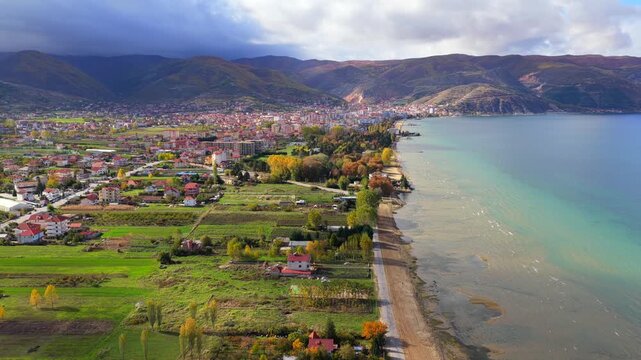 Aerial video of Pogradec town along Lake Ohrid with mountains, green fields and dramatic clouds.