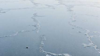 Thin cracks forming on frozen lake surface during winter sunset