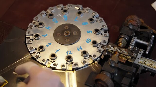 Close-up of a precision mechanical indexing machine with a numbered rotary plate, clamps, geared feed, and micrometer adjustment, operated by hand during metalworking setup.