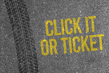 Tire track on asphalt background with yellow text Click It Or Ticket. Road safety and seat belt concept.