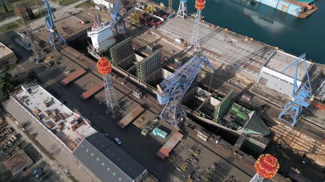 Aerial view of a ship repair yard with dry docks, cranes, and cargo vessels in an industrial port. Large shipyard infrastructure, maritime industry, logistics and repair operations by the water