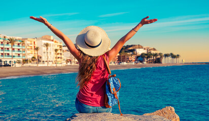 Woman sitting on a rock with raised arms overlooking a city in Andalusia, Spain