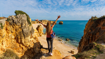 Happy woman tourist enjoying panoramic view of beach, sea and roch, famous beach in Algarve, Portugal