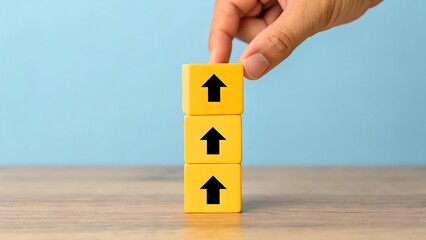 Hand adjusting stack of yellow cubes with upward arrows on wooden surface
