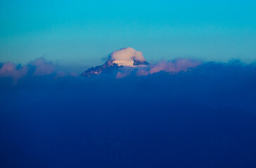 Clouds surround the peak of a mountain in the background. The sky shows clear blue with shades of pink as the sun begins to set in the late afternoon.