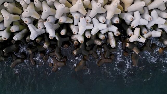 Aerial video of concrete tetrapods forming a breakwater as waves crash against the coast. Abstract geometric pattern, coastal protection infrastructure, sea and motion