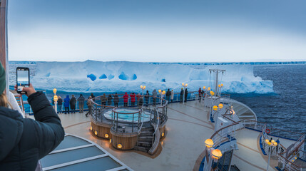 Antarctica - January 10 2024 - Photo of A23a Iceberg from Cruise Ship Behind Crowd. Female Passenger Holds Mobile Phone Takes Photo © And They Travel