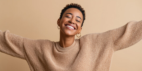 Joyful smiling woman with short natural hair and open arms in a cozy beige sweater conveying happiness, confidence and positive lifestyle.