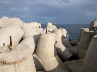 Concrete wave breakers stacked along the shoreline, forming a massive coastal defense structure against sea waves. Industrial geometry, repetition, and texture at the water s edge