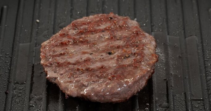 Raw beef burger patty cooking, frying on grill pan, skillet. Chef flipping burger cutlet while cooking.
