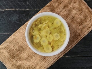 Fresh sliced baby corn soup in a white bowl on burlap and dark wooden background. top view 