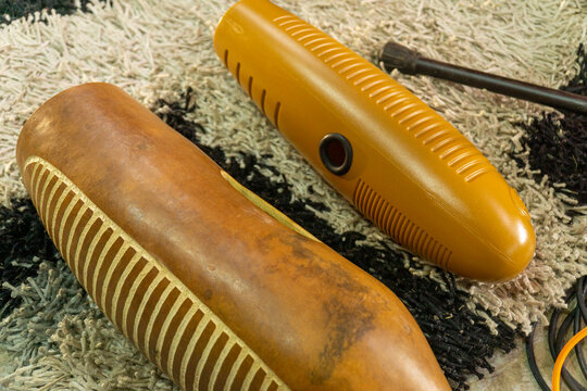 Pair of musical guiros, one natural wood and one yellow plastic, on a textured rug, representing traditional percussion instruments.