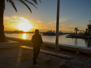 Vilamoura Marina, Algarve, Portugal at sunset, a line of boats and yaghts moored against a jetty, the sky and the water are lit bright orange by the setting sun