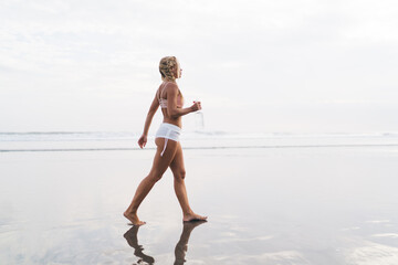 Mindful woman walks along shoreline with water bottle, symbolizing calm energy, hydration, and strength of body and mind through movement