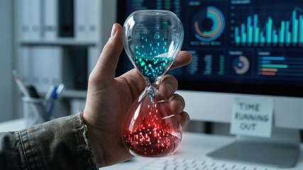 Hand holding hourglass with digital particles symbolizing ai risk controls and time running out in front of computer screen with data charts