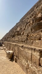 Tourists explore the ancient pyramid at Giza under a bright sky, walking along the stone steps and examining the large pyramid structure and stonework as a historic landmark