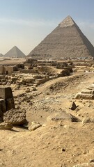 Visitors explore the Giza plateau where large pyramids rise above the sandy ground. Ancient stones lie near paths, showing signs of past human activity under the sun