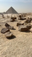 Stone blocks are scattered on the ground near the Great Pyramid of Giza. People walk and explore around the historical site under a clear sky in the daytime