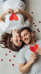 Young couple lying together and holding red hearts on floor  