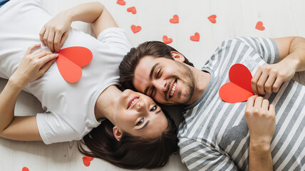 Young couple lying on the floor holding heart shapes for Valentine's Day  