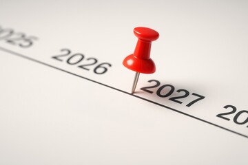 Red pushpin marking year 2027 on calendar symbolizing goal setting and budget planning for 2026 with clear focus on future success and achievement