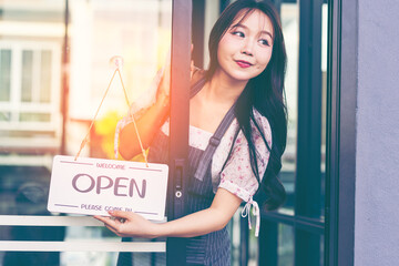 Female owner of coffee shop or restaurant turning round sign to open. Smiling young asian woman owner, employee retail coffee shop woman hand in setting sign board to open for welcome customer, reopen