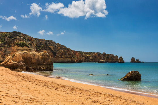 A stunning and iconic view of Praia dos Tr&ecirc;s Irm&atilde;os in the Algarve, Portugal, showcasing its breathtaking golden sand beach framed by towering, dramatic limestone cliffs.