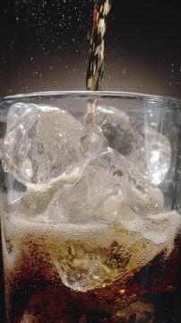 Close-up shot of cola being poured into a glass on the table with visible foam, fizz and rising carbonate bubble. Close-up.
