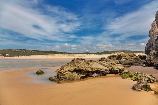 A breathtaking panoramic view of Praia da Amoreira in the Algarve, Portugal, showcasing its vast expanse of golden sand stretching toward distant dunes and lush green hills