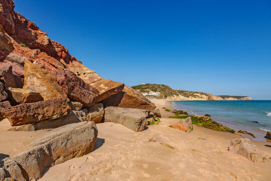 A stunning view of Praia da Salema in the Algarve, Portugal, where golden sands meet the turquoise waters of the Atlantic Ocean under a brilliant blue sky.