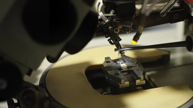 Precision station examining a semiconductor microchip under microscope illumination, with robotic micromanipulators aligning fine probes onto contact pads for electronic testing.