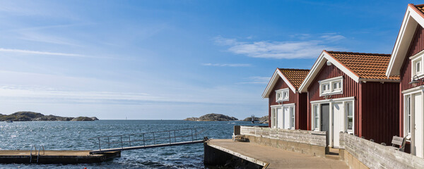 Charming red wooden cottages by the sea on island Tjorn, Sweden with a wooden pier and calm blue water © Hilda Weges